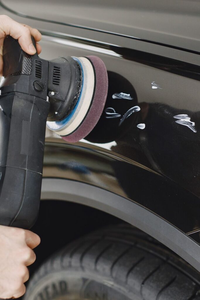 Hands using a polishing machine on a car's surface in a garage setting.